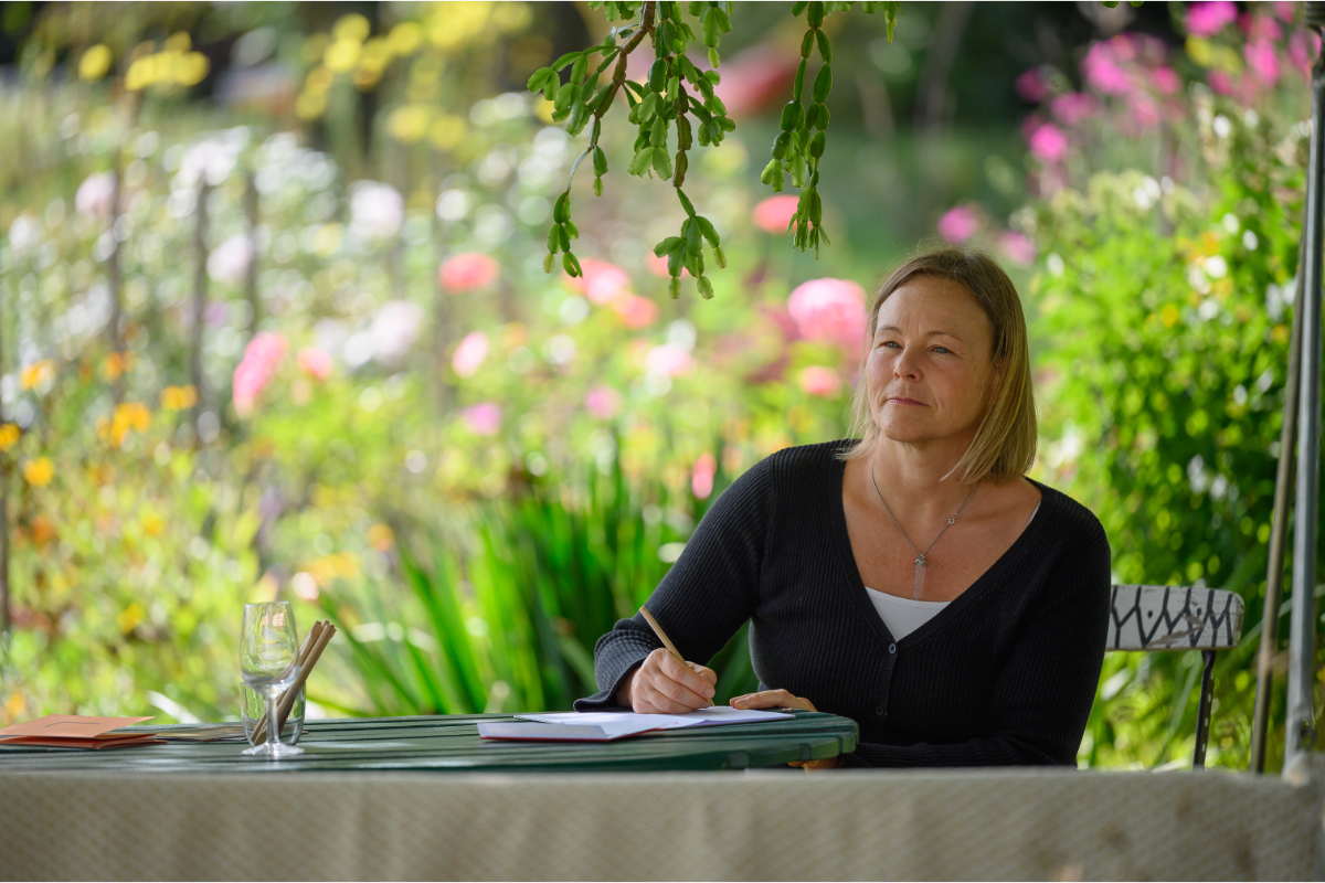 Eine Hörerin schreibt im weitläufigen wilden Garten des Forsthauses ihren „Liebesbrief“ an die Musiker:innen.